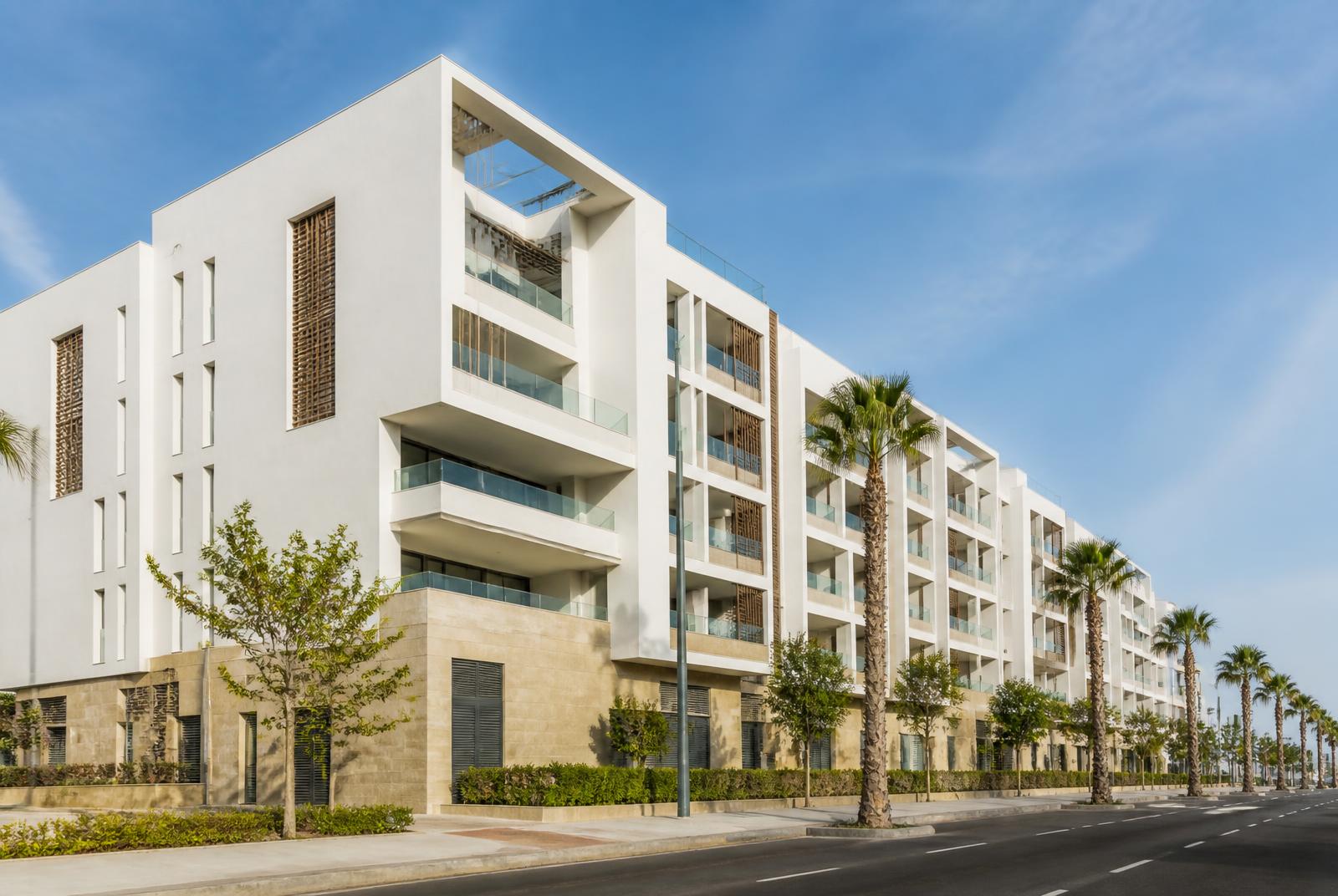 Modern wit wooncomplex in Casablanca met diepe balkons, natuurstenen plint en palmen langs de straat